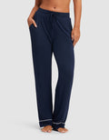 A woman wears HIDE Women's Bamboo Stretch-Knit Pajama Pant in navy, featuring white piping near the ankles, standing barefoot with hands in pockets against a plain light background. |Color:Navy